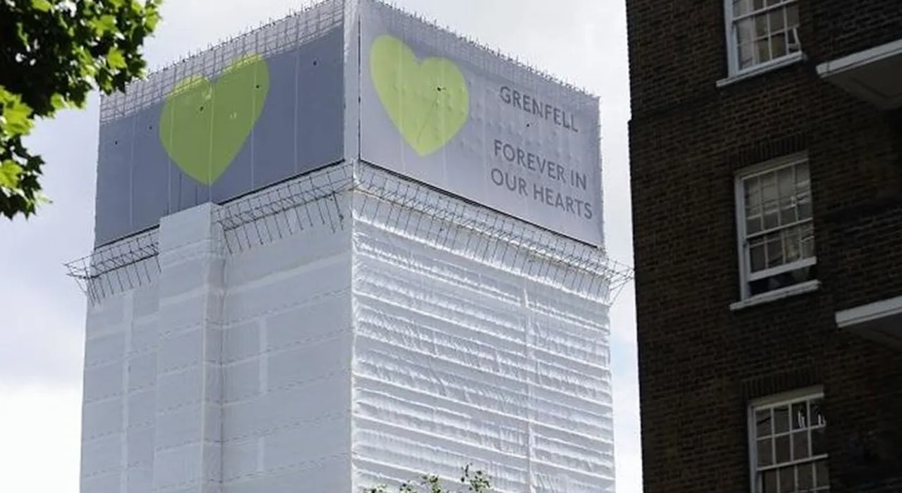 Grenfell Tower wrapped in white sheeting, with two large green hearts and the words "Grenfell Forever in Our Hearts."