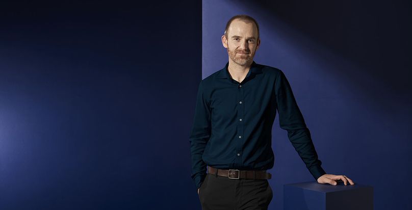 Dan Craig standing against a dark blue backdrop