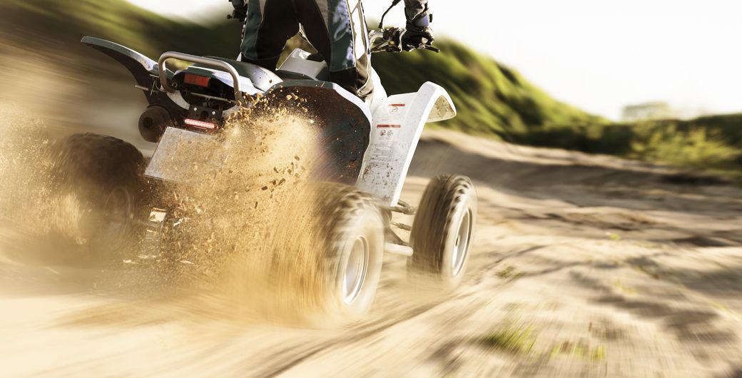 A quad bike kicking up sand on a dirt track