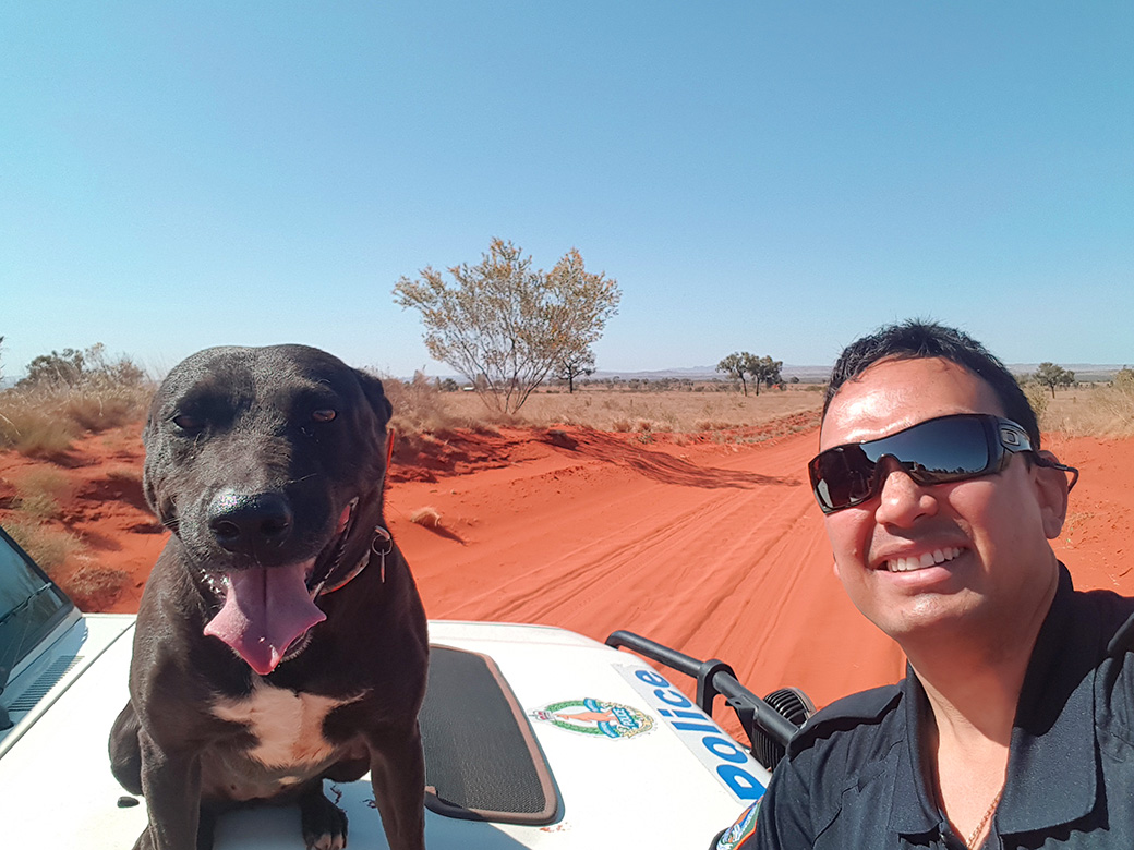 Alphonsus Shields with a dog on the bonnet of a police vehicle on a red dirt road in the Northern Territory