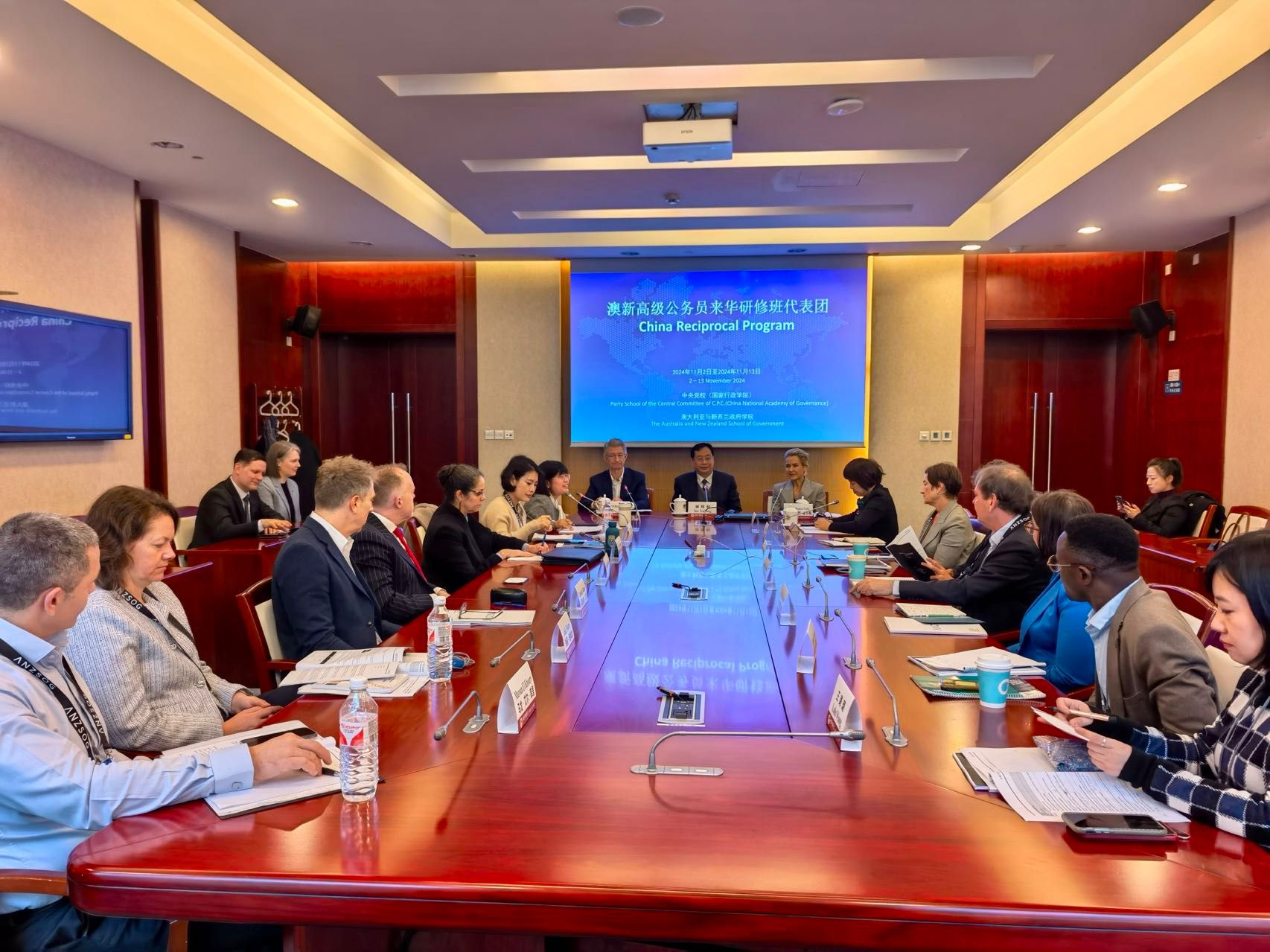China Reciprocal Program participants and hosts seated around a long conference table beneath a screen showing the program title