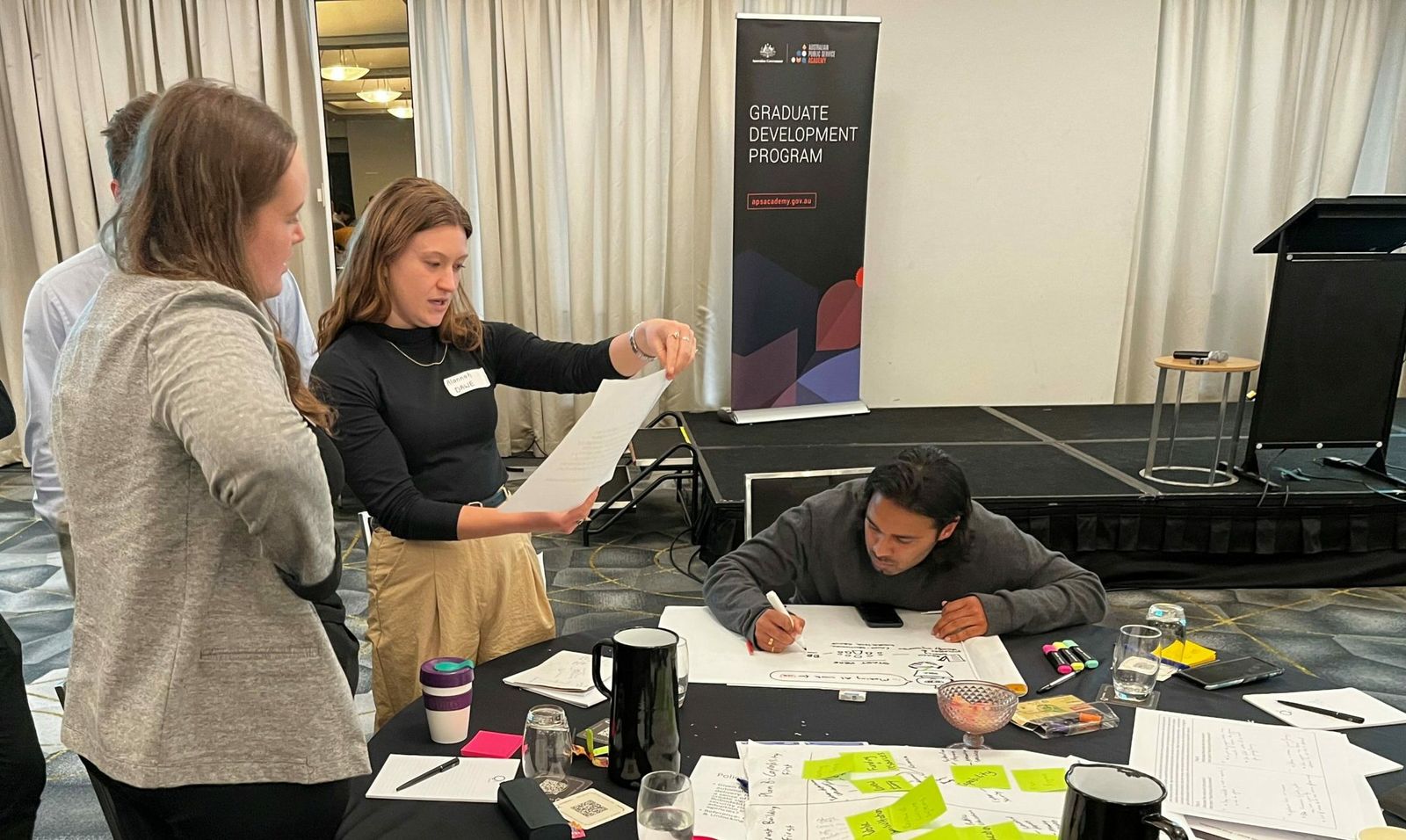 APS graduates working on ideas with sheets of paper and sticky notes at the ANZSOG policy hackathon