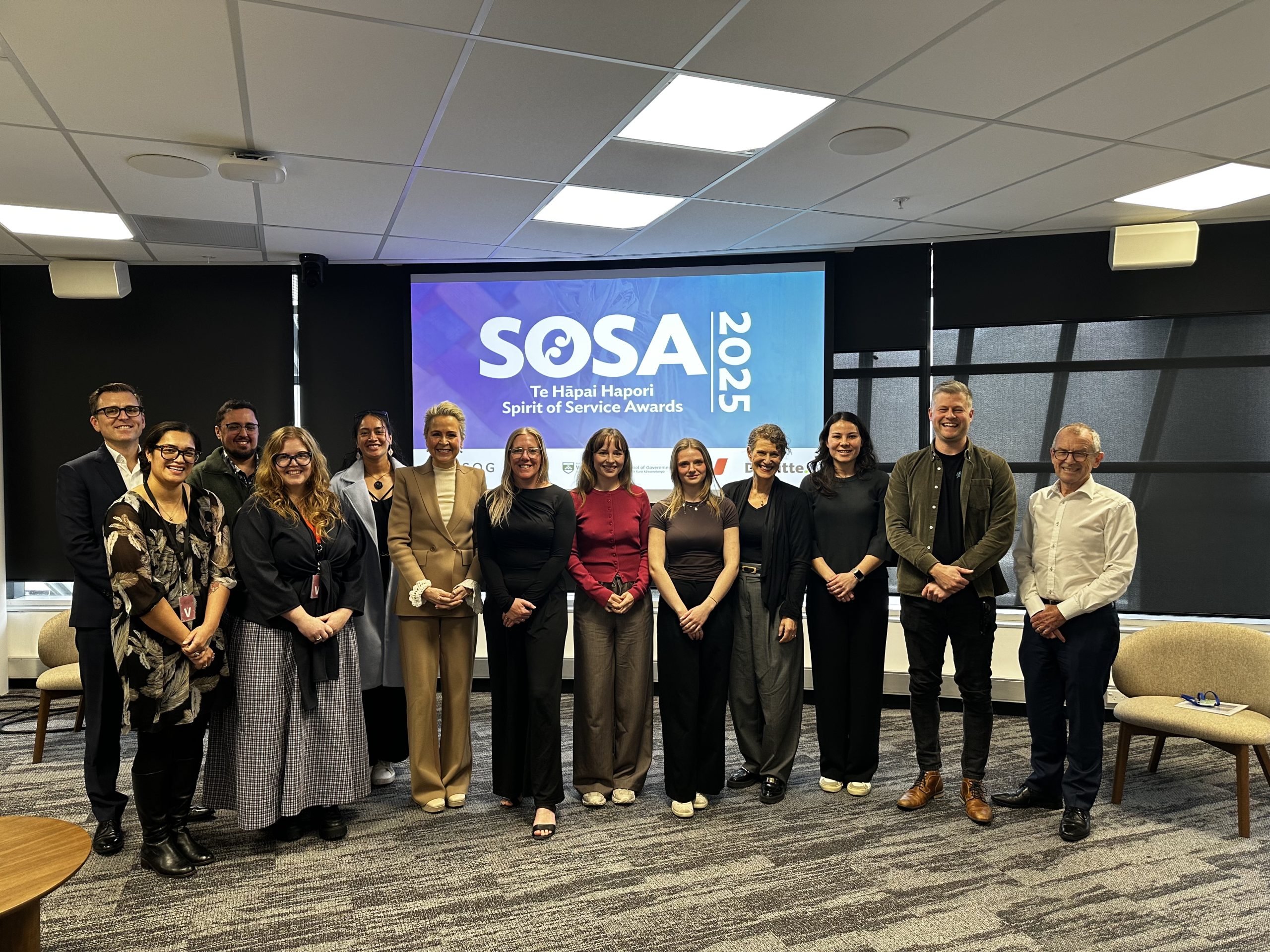 Group of award attendees standing in front of a screen reading 'SOSA 2025 Te Hāpai Hapori Spirit of Service Awards'