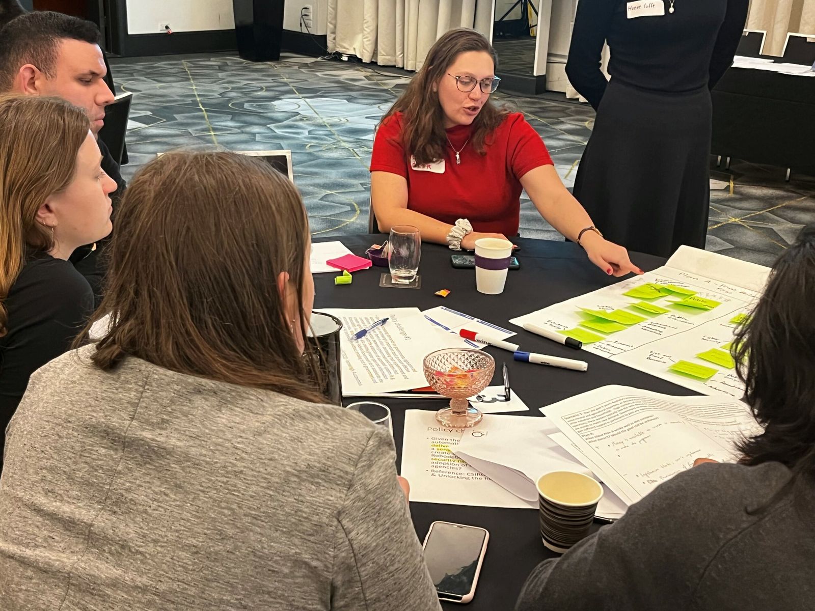 A facilitator talks through sticky-note ideas with APS graduates around a table at the policy hackathon