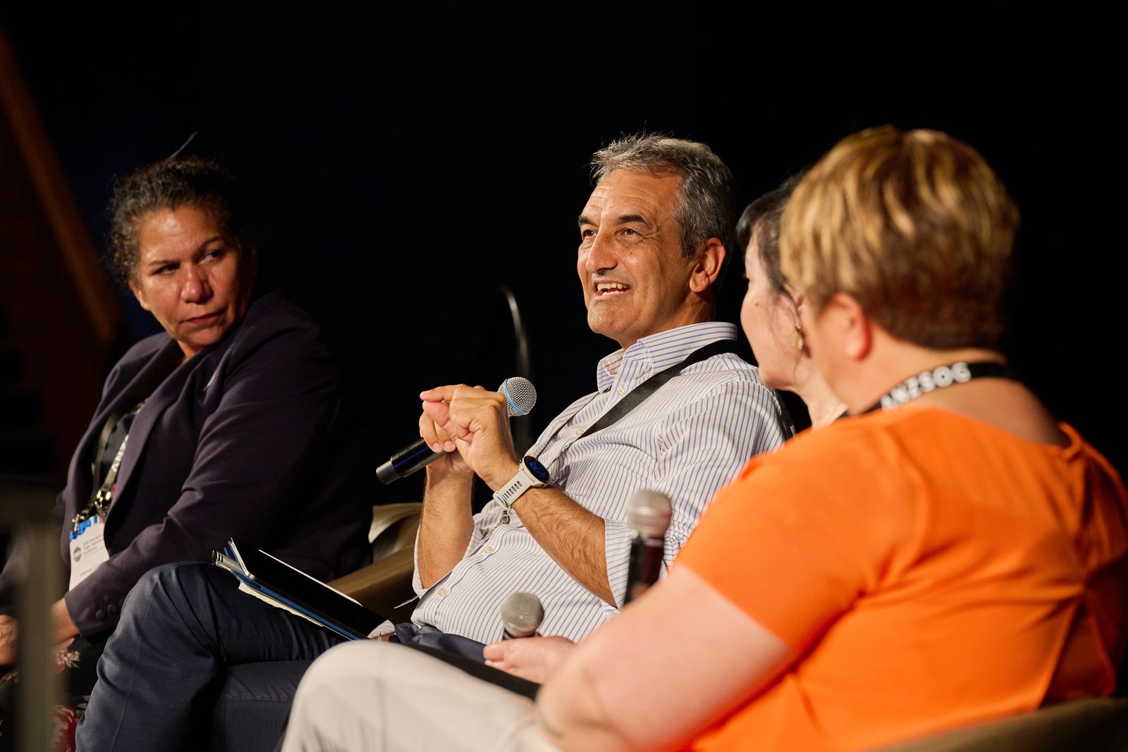 Panellists in conversation on stage at the ANZSOG First Nations conference, a man smiling as he speaks into a microphone