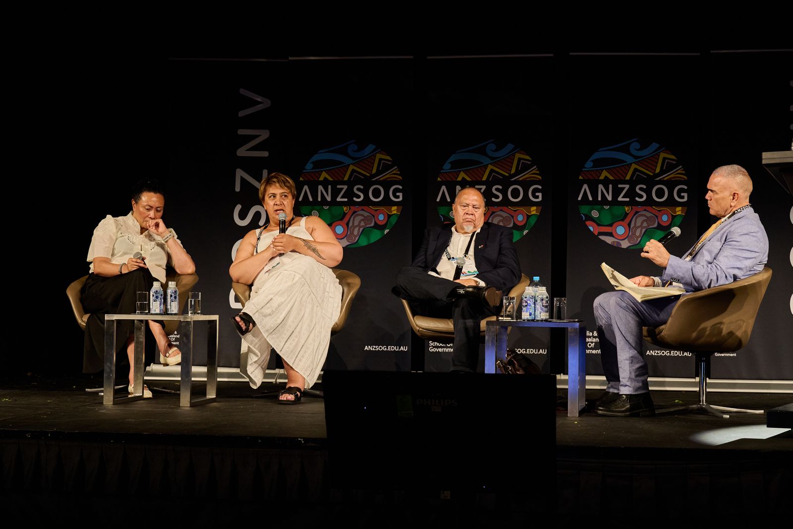 Four panellists seated on stage in front of ANZSOG banners at the First Nations conference, one speaking into a microphone
