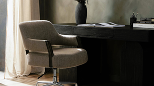 A modern office setup with a beige swivel chair, a dark wooden desk with books, a vase, and a pen holder, against a softly lit background.