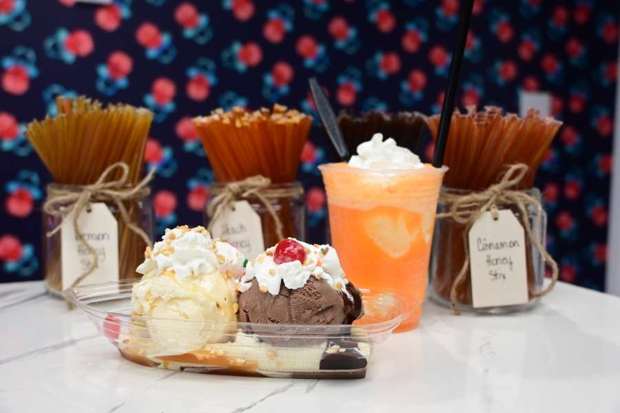 A dessert display featuring ice cream sundaes, pasta utensils in decorated jars, and a colorful orange beverage.