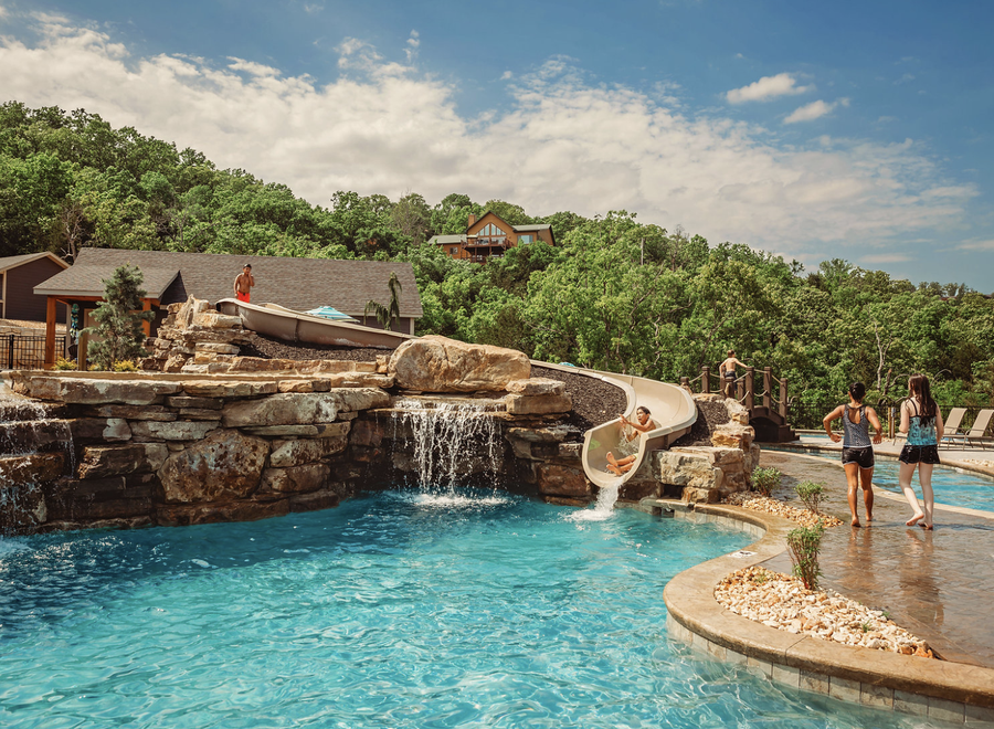 # ALT Text:

Luxury resort pool with waterslide, waterfall, and families enjoying recreational activities surrounded by trees.
