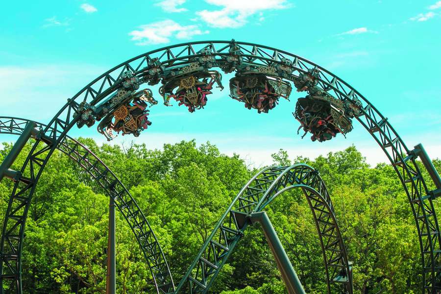 A thrilling roller coaster with ornate cars suspended upside down against a bright blue sky.