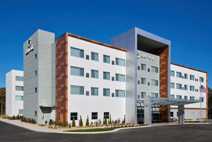 Modern multi-story hospital building with white and copper exterior, featuring glass windows and American flag.