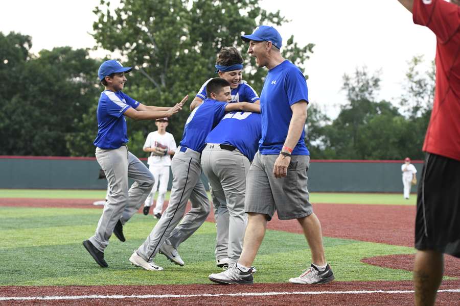 Youth baseball coach celebrates with young players on field during team practice session.