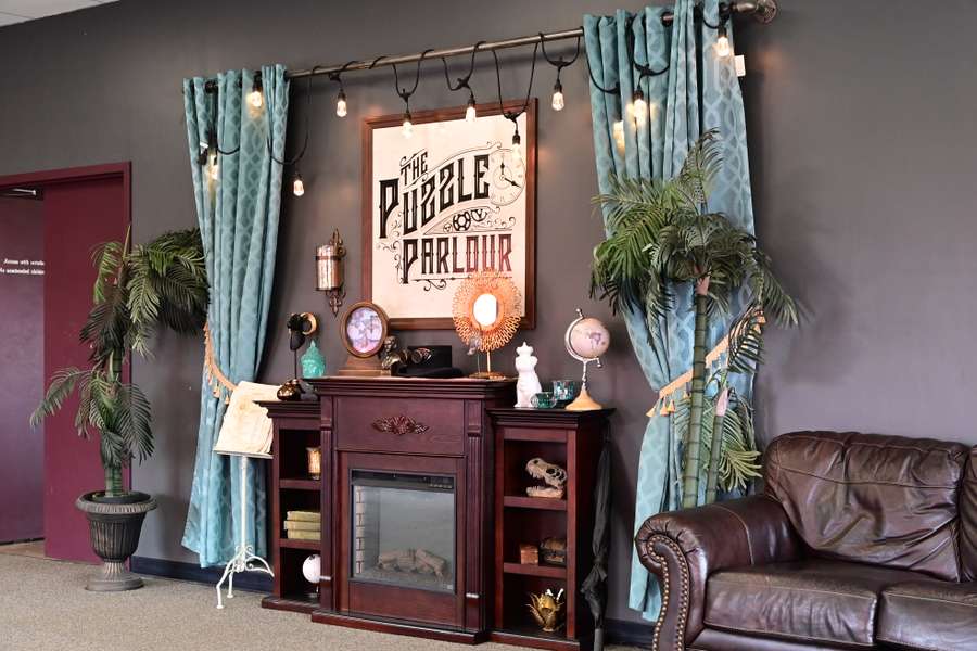 A Victorian-style parlor featuring a fireplace, teal curtains, plants, leather sofa, and vintage decor.