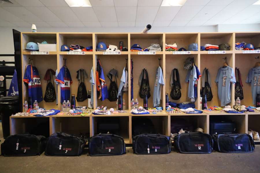 A sports locker room with wooden cubicles displaying jerseys, equipment, bags, and personal gear for team members.
