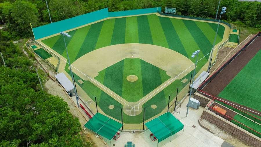 Aerial view of a well-maintained baseball field with striped outfield grass and dirt infield surrounded by green fencing.