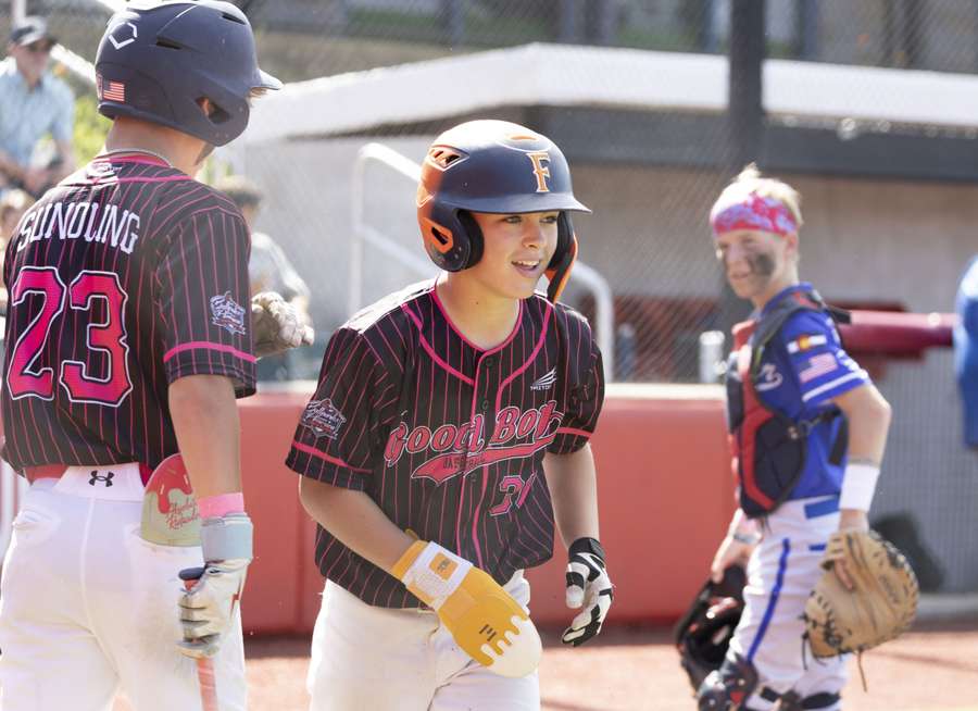 Young female baseball players in maroon pinstriped uniforms celebrate during a game at home plate.