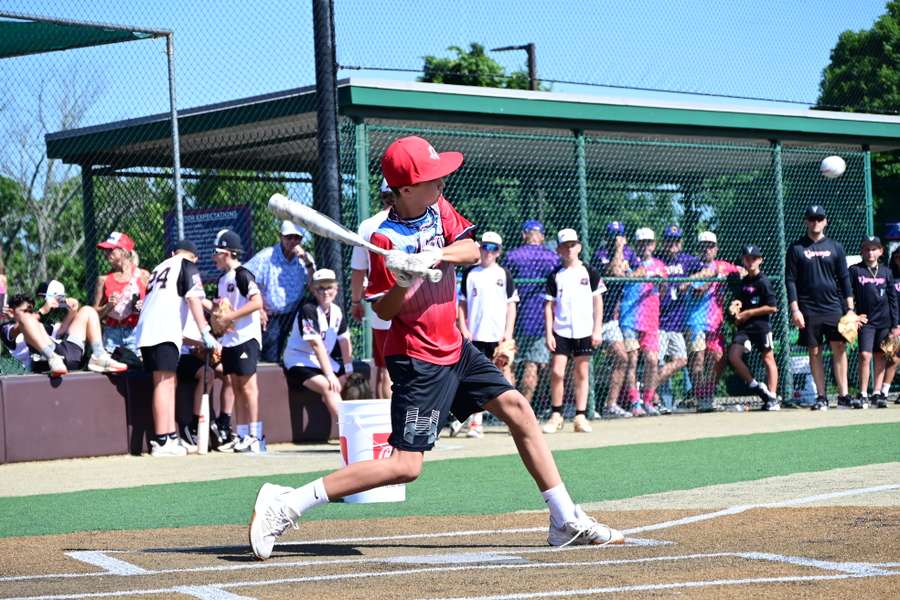 Young baseball player in red uniform swings bat at ball during youth tournament game.