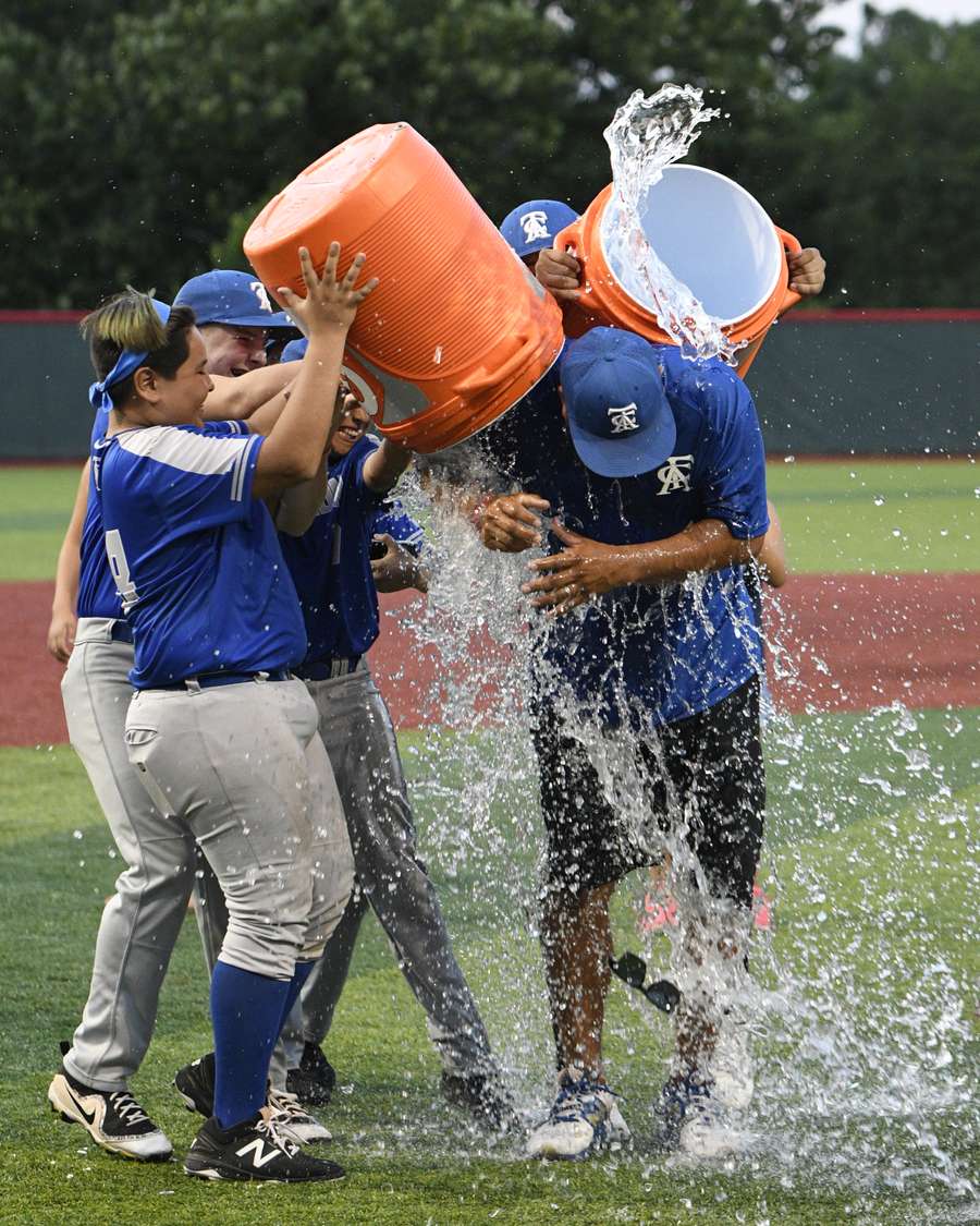 Young baseball players in blue uniforms celebrate with water bucket splash on field.