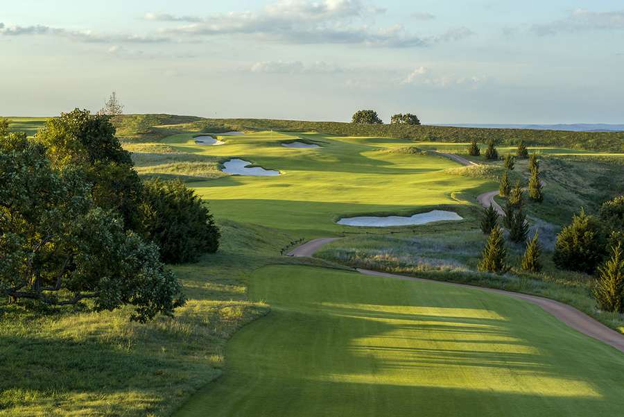 A scenic golf course with rolling green fairways, bunkers, water hazards, and surrounding trees.