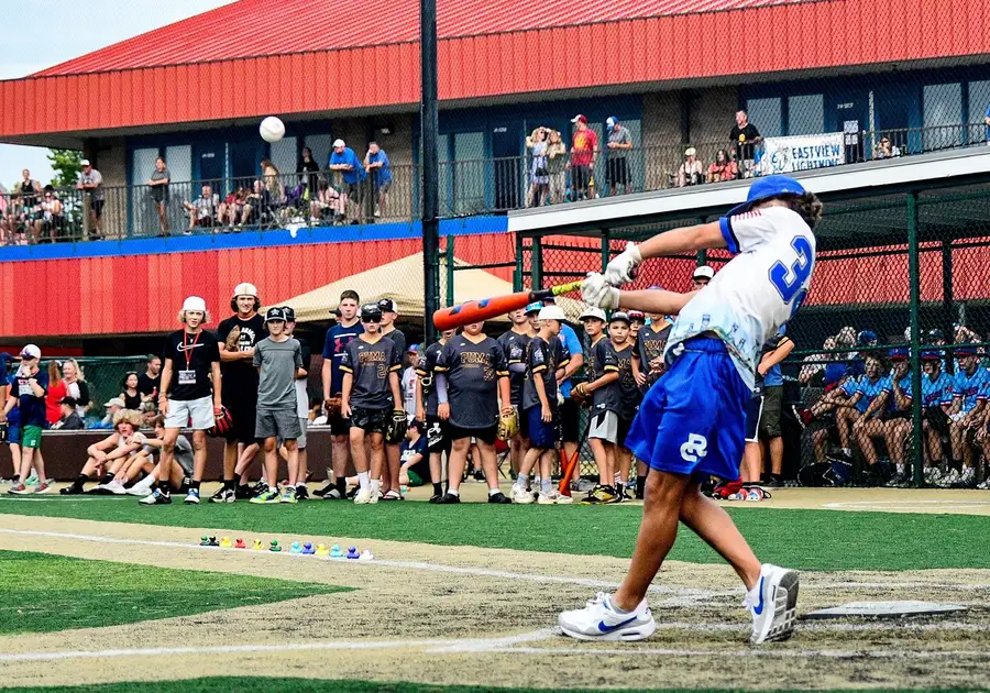 Young baseball player in blue uniform swings bat during game at stadium.