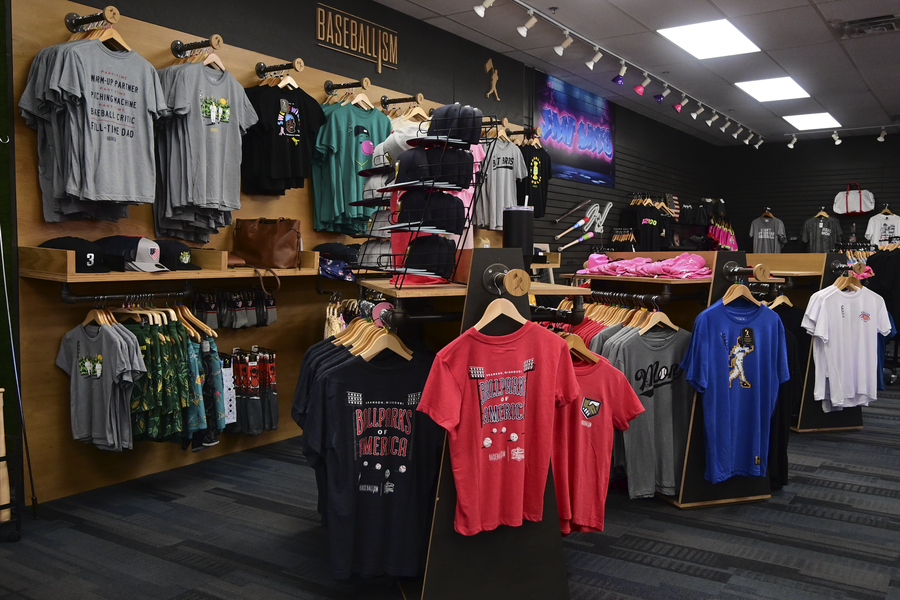 Baseball-themed retail store displaying merchandise including t-shirts, jerseys, helmets, and wooden hangers.