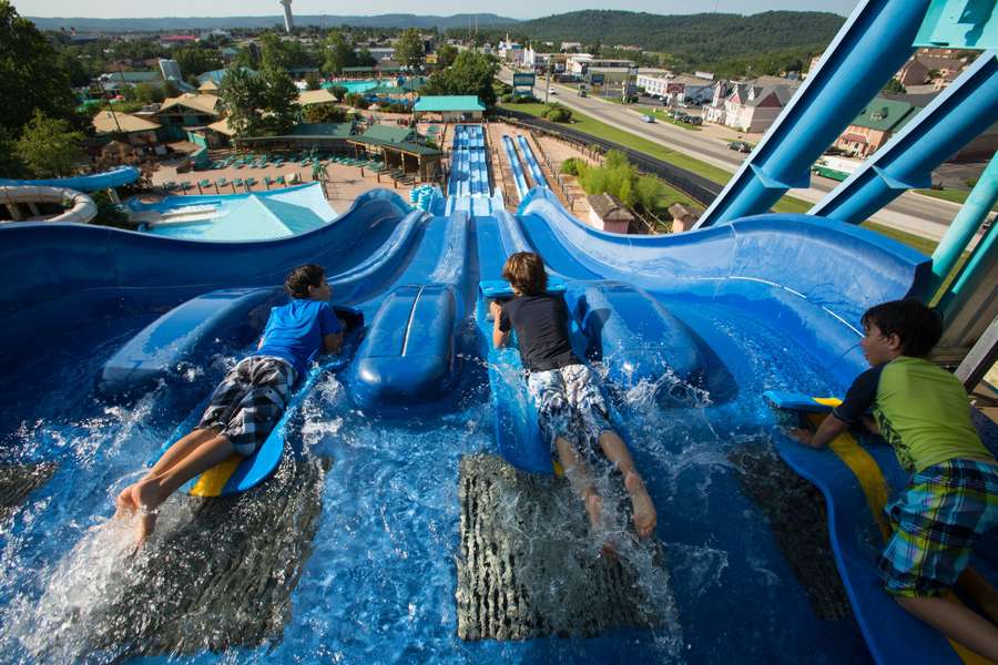 Children sliding down multiple blue water slides at an outdoor amusement park on a sunny day.