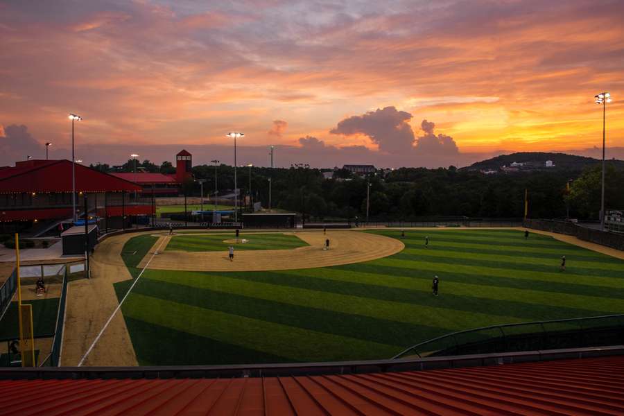 A baseball field at sunset with players scattered across the grass and infield during evening practice.