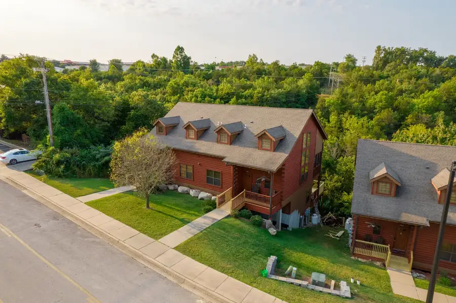 Aerial view of a red wooden two-story house with gray roof surrounded by green trees and lawn.