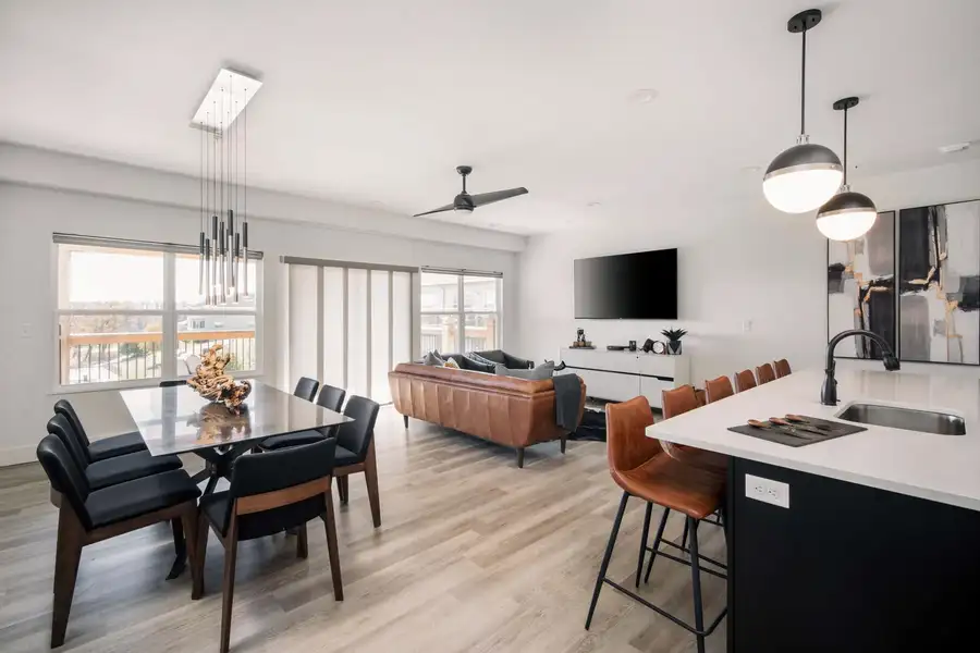 Modern open-concept apartment with dining area, kitchen island, living room, and large windows overlooking city.