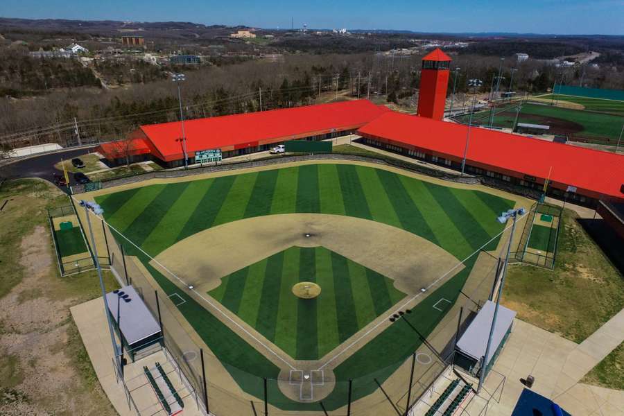Aerial view of a modern baseball field with bright red roof buildings and manicured grass.