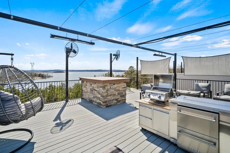 Luxury rooftop deck overlooking a lake with outdoor kitchen, grill, and shade structures.