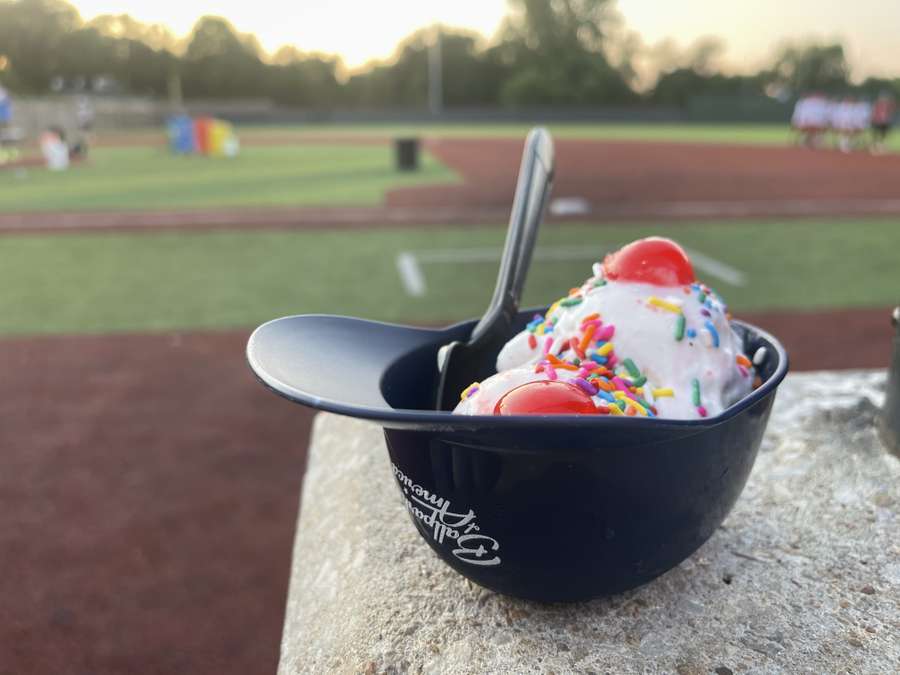 Two ice cream cones with red cherry toppings and colorful sprinkles in a black bowl at a sports field.