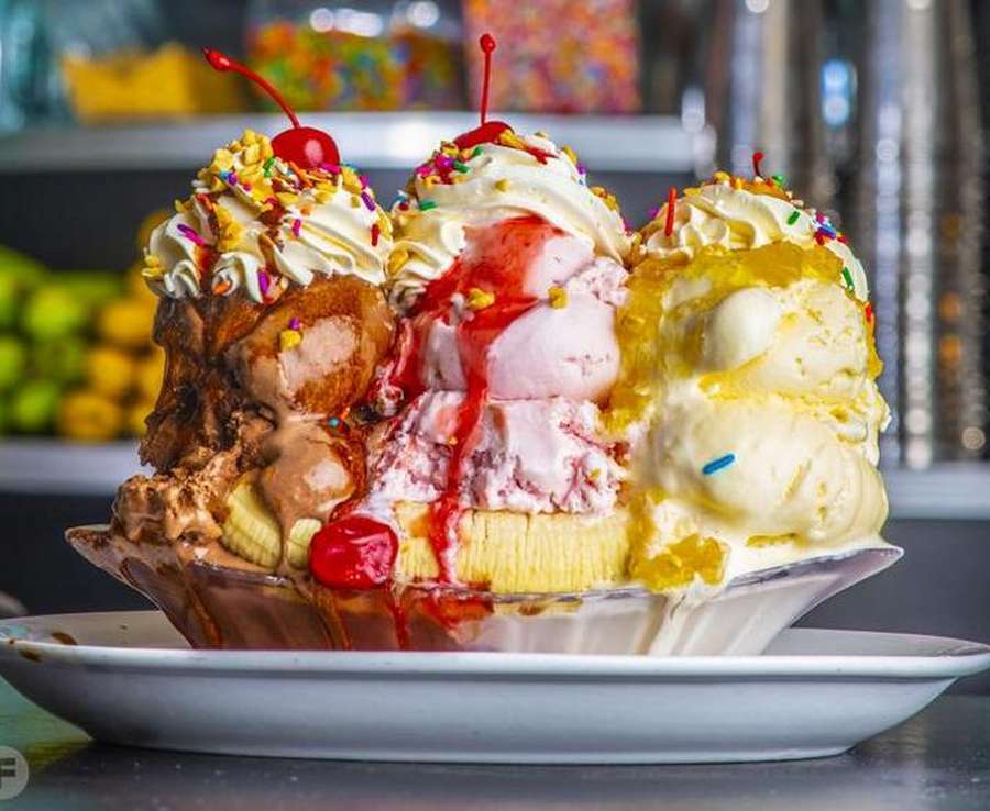 Three decadent ice cream sundaes with colorful sprinkles, whipped cream, and maraschino cherries on plate.