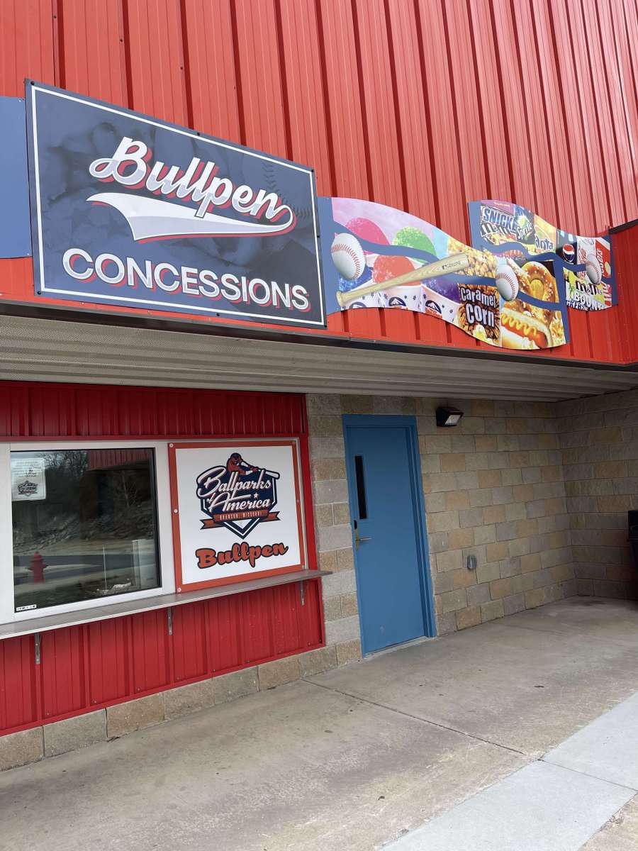Bullpen Concessions stand with red metal exterior and signage displaying snacks and baseball-themed branding.