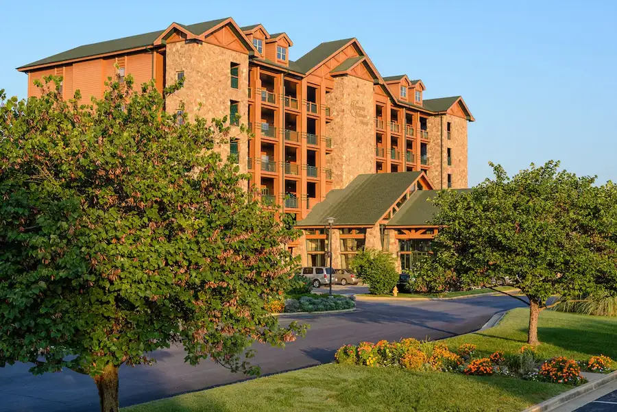 Large orange brick hotel with green roofs surrounded by landscaped grounds and trees.