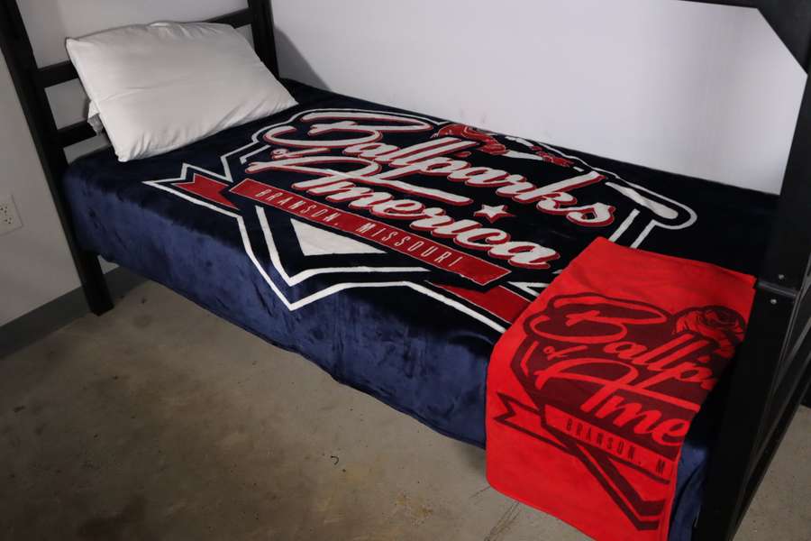 A bed with black metal frame featuring Harley-Davidson themed bedding in red, white, and navy blue colors.