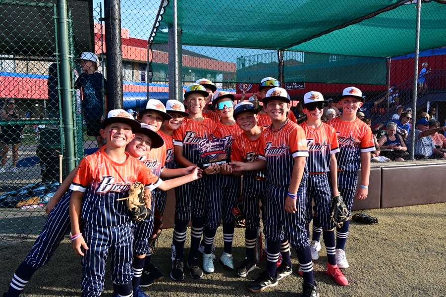 Young baseball team in red and navy uniforms smiling together at the field.