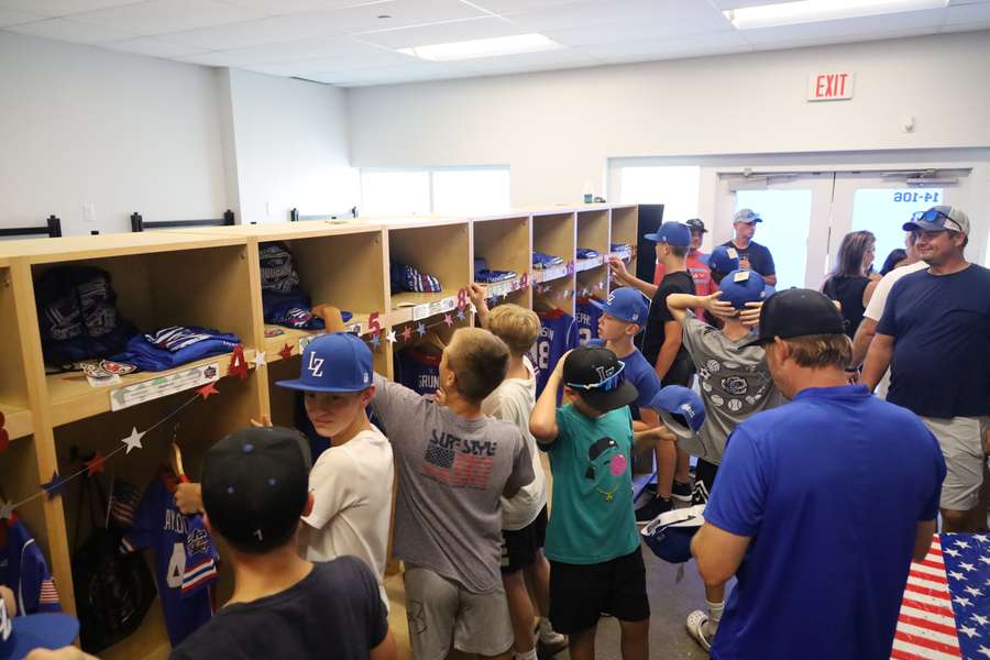A crowded locker room tour where children and adults examine blue sports uniforms and equipment displayed in wooden shelves.