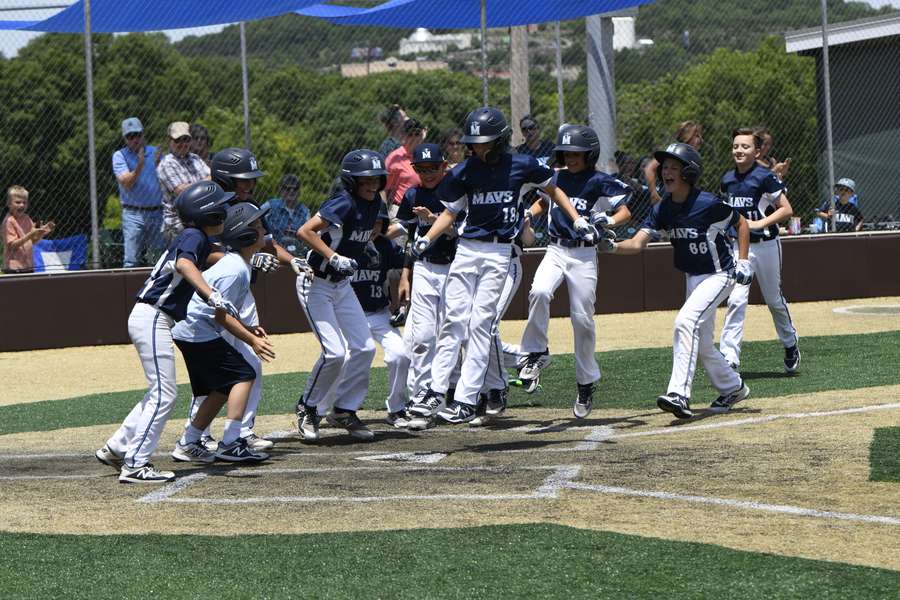 Young softball players in Mavs uniforms celebrate at home plate during a game.