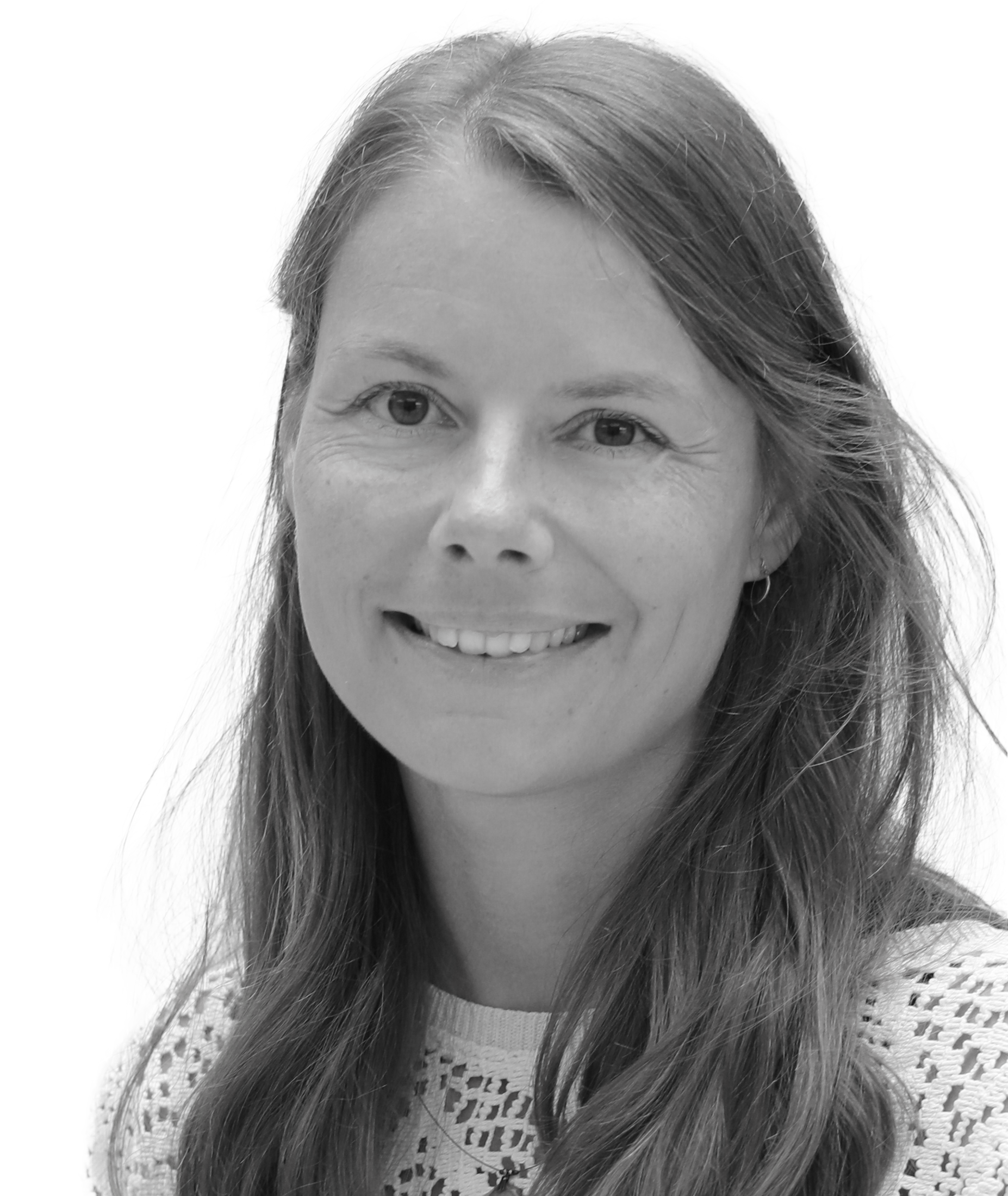 A woman with long hair and a gentle smile, wearing a lace-patterned top, is seen in a close-up black and white portrait.
