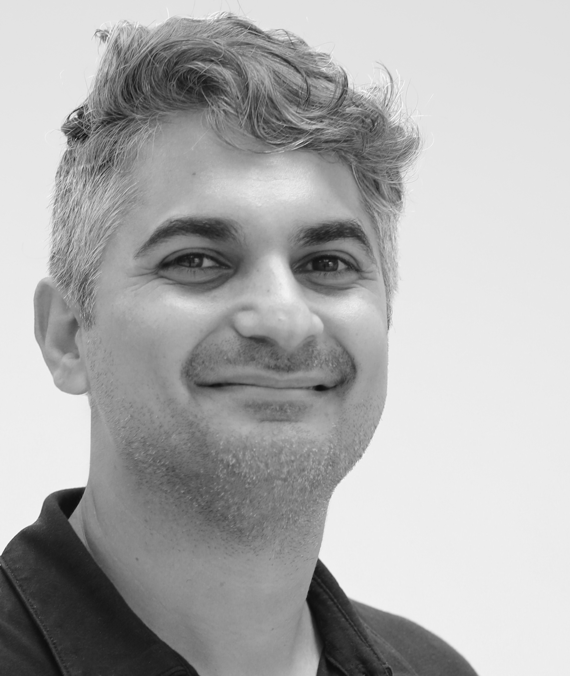 Black and white portrait of a smiling person with short, wavy hair, wearing a dark shirt, against a plain background.