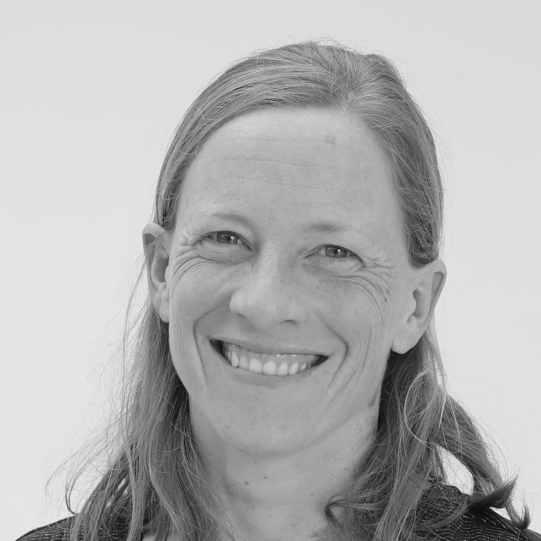 Smiling woman with long hair in a black and white portrait against a plain background.