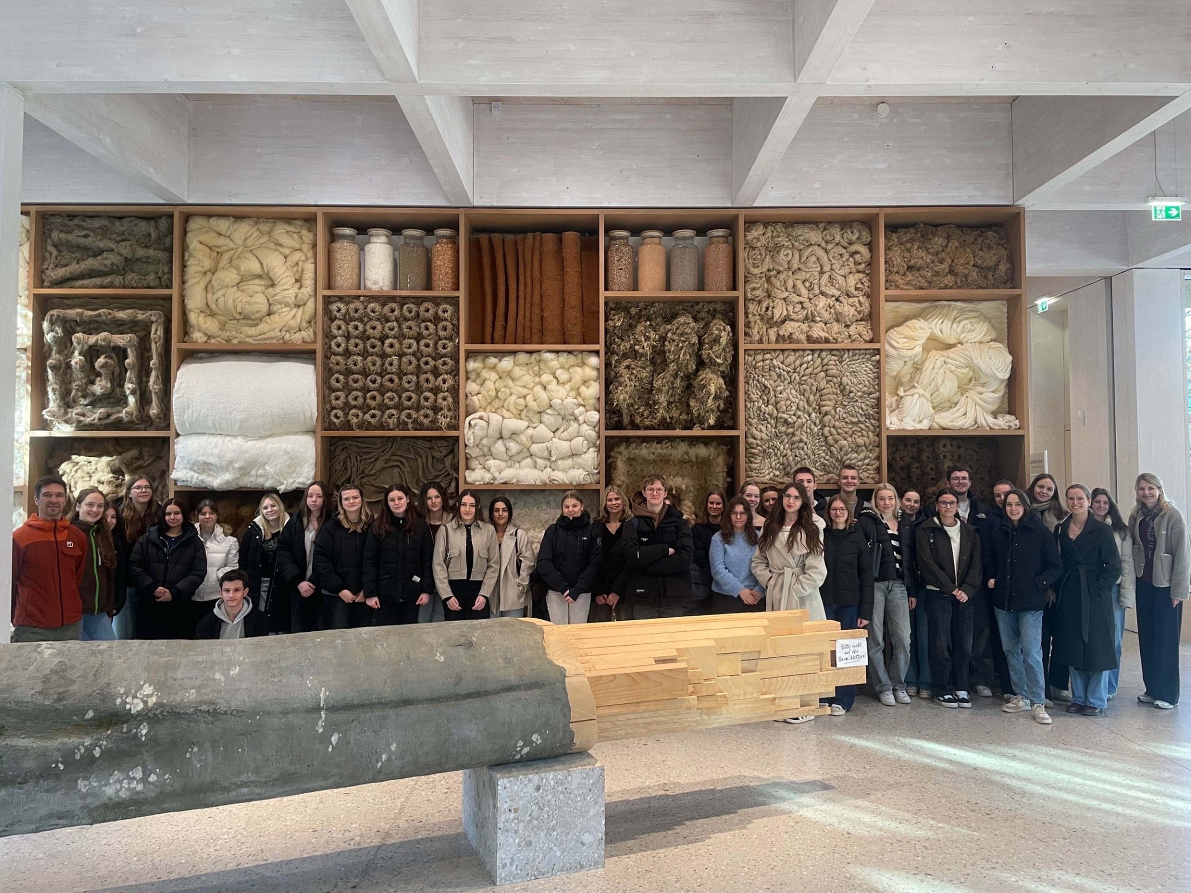 A large group of people poses in front of a wall display featuring various textile materials in a modern museum setting.