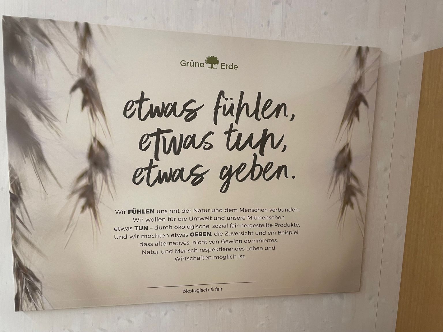 A sign with German text promoting environmental and social responsibility, featuring a blurred image of wheat in the background.