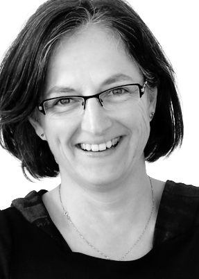 Smiling woman with shoulder-length dark hair and glasses, wearing a dark top.