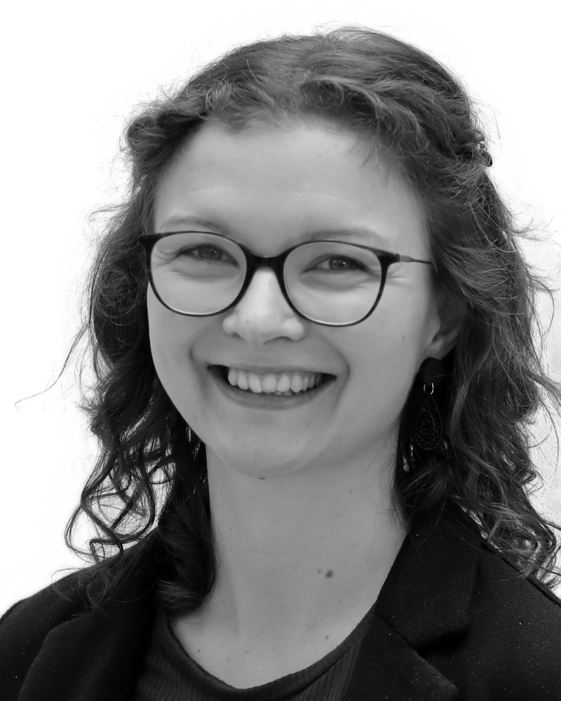 A smiling person with curly hair, wearing glasses and a blazer, in a black and white portrait.