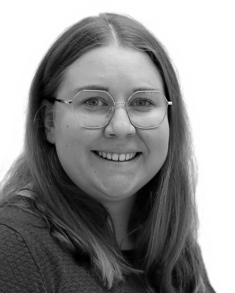 A black and white portrait of a smiling person with long hair and glasses against a white background.