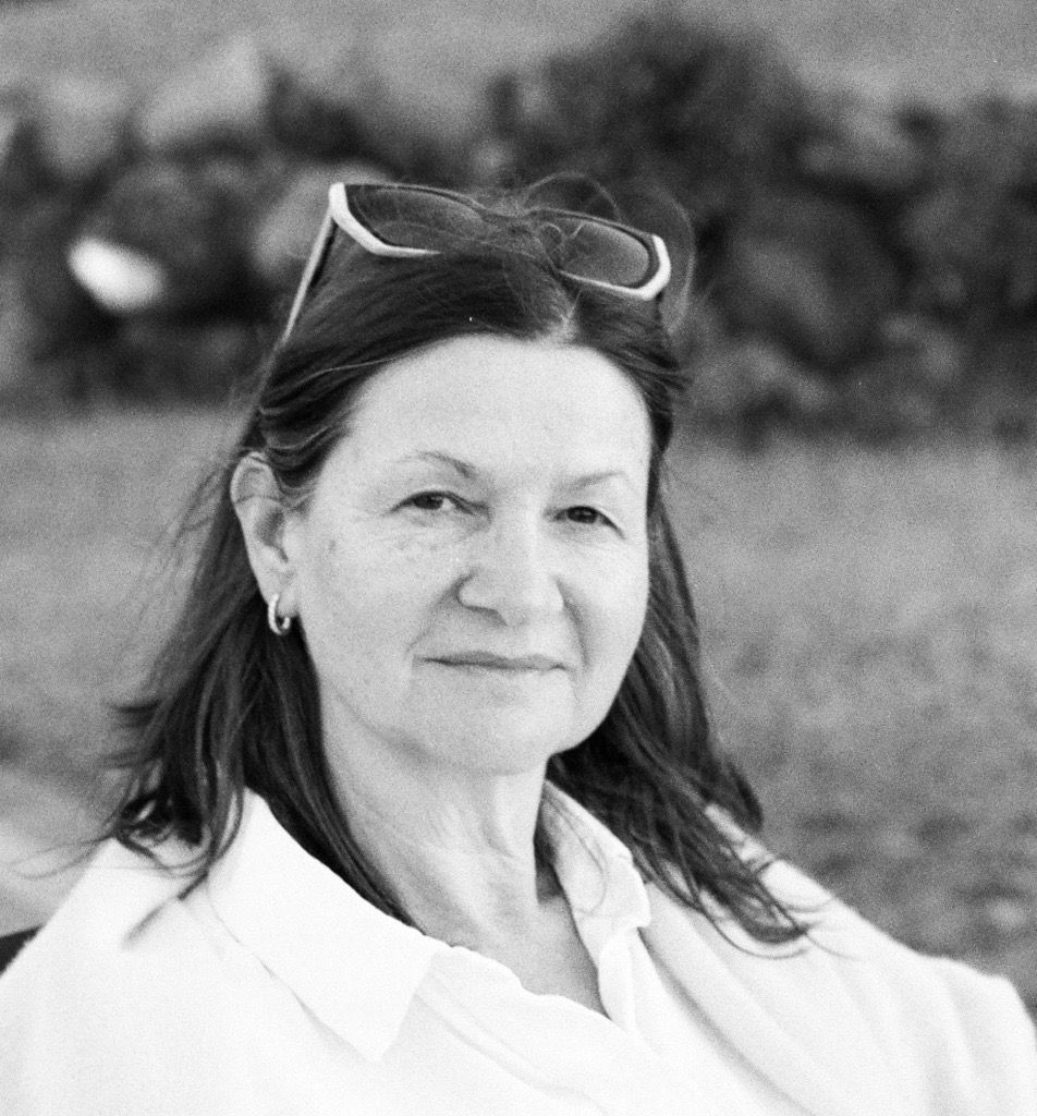 Black and white portrait of a woman outdoors, wearing glasses on her head, looking at the camera with a neutral expression.