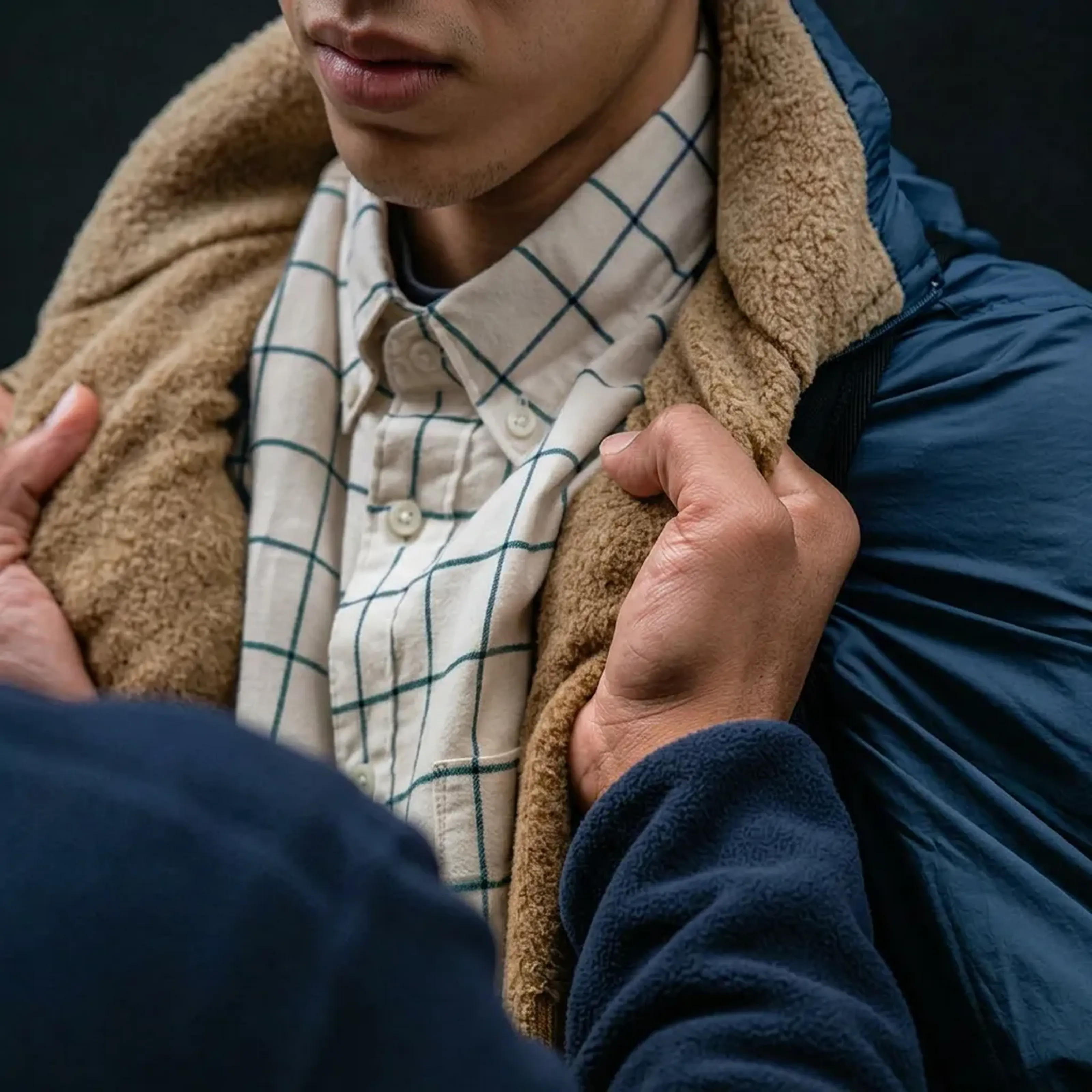 Eine Person in kariertem Hemd und Jacke mit flauschigem Kragen wird an der Jacke festgehalten.