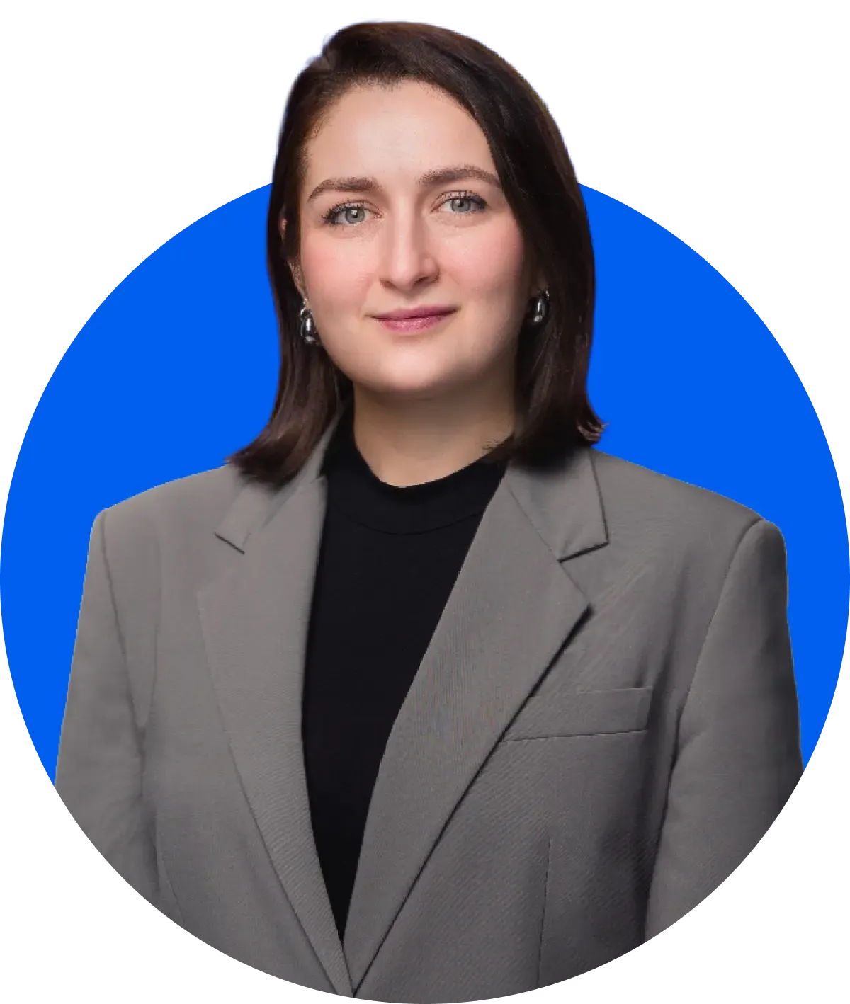 Eine Person mit kurzen Haaren in einem grauen Blazer und einem schwarzen Oberteil, die vor einem blauen, runden Hintergrund steht.